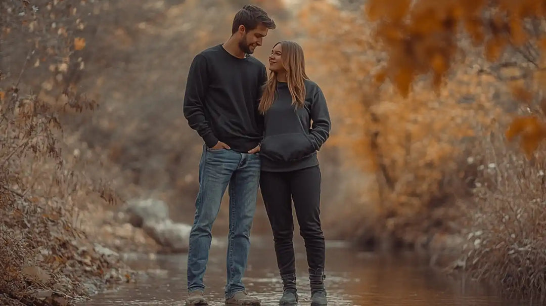 A couple in dark sweaters standing close together by a stream.